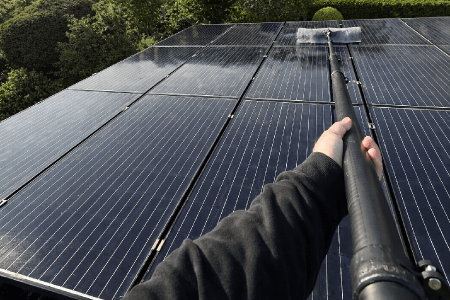 Ein Mann reinigt mit einer langen Teleskopstange und einem Bürstenaufsatz Solarpaneele